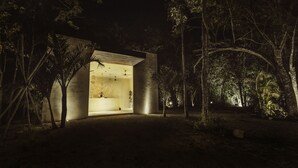 Um edifício moderno e iluminado com fachada de vidro, rodeado por uma floresta densa.