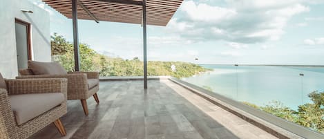 Un área de estar al aire libre techada con muebles de mimbre y vistas al mar, con un estilo arquitectónico moderno.