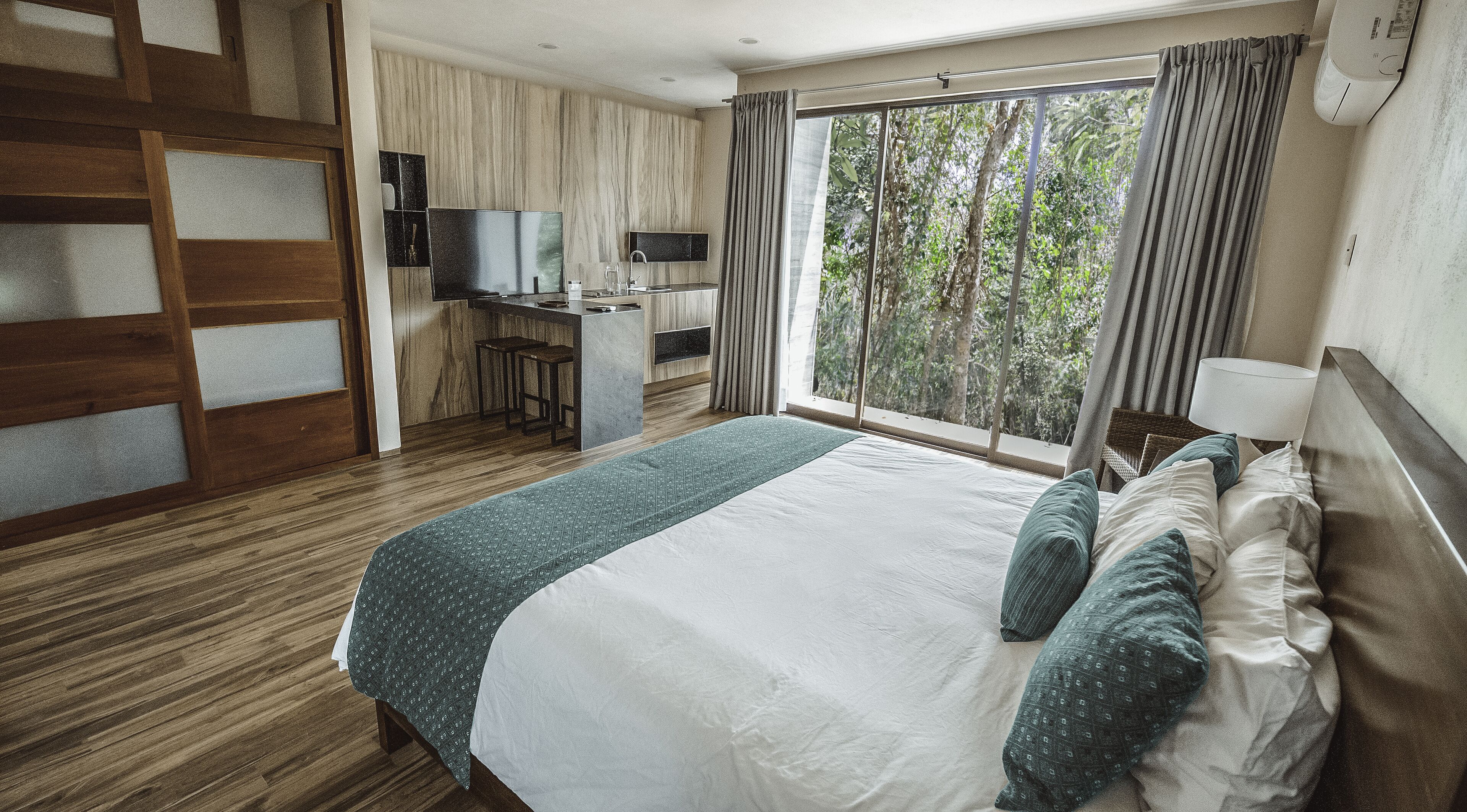 A hotel room with a large bed, a desk with a chair, a television, and a window with curtains.
