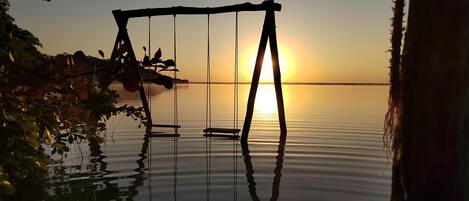 A swing set over calm water with a sunset in the background.
