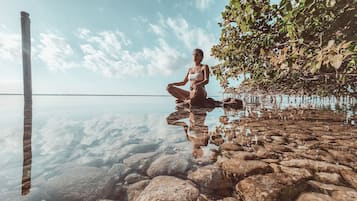 Una persona sentada sobre rocas junto a un cuerpo de agua tranquilo, con cielos despejados.