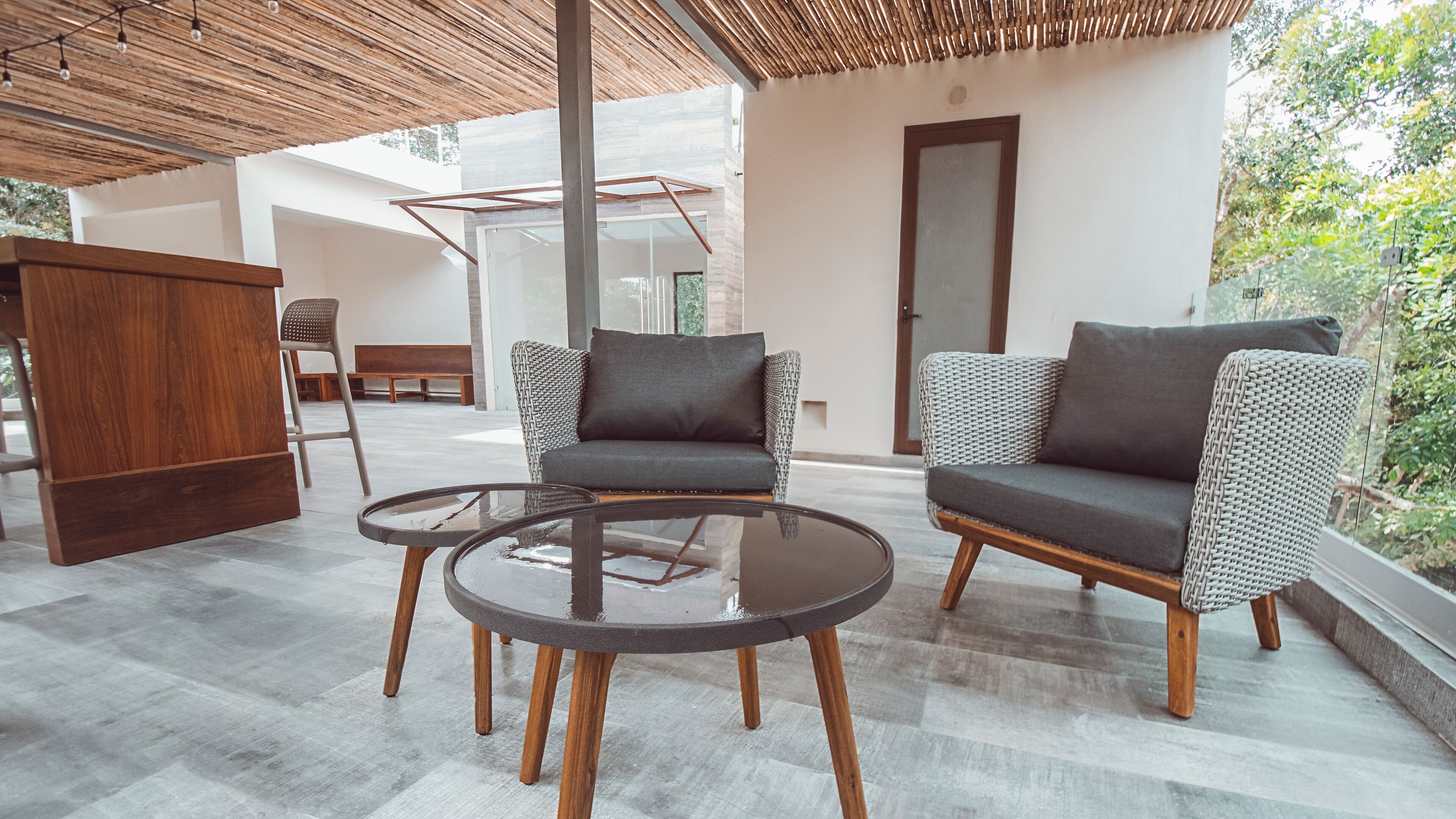 Un área de estar exterior moderna con dos sofás y una mesa de vidrio, rodeada por una pérgola de madera y vistas a un jardín.
