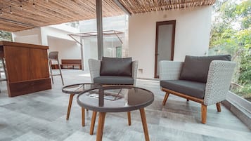 Un área de estar exterior moderna con dos sofás y una mesa de vidrio, rodeada por una pérgola de madera y vistas a un jardín.
