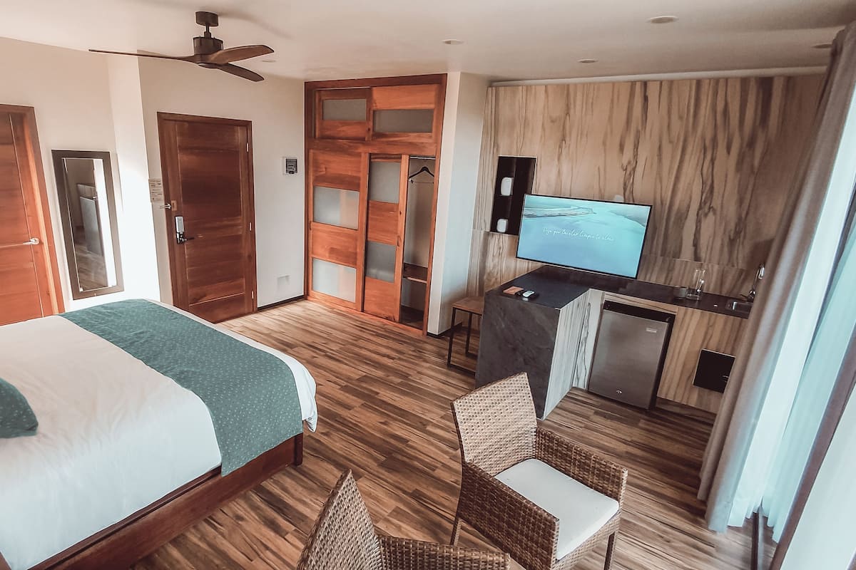 A hotel room with a bed, a desk with a TV, a ceiling fan, and a wardrobe.