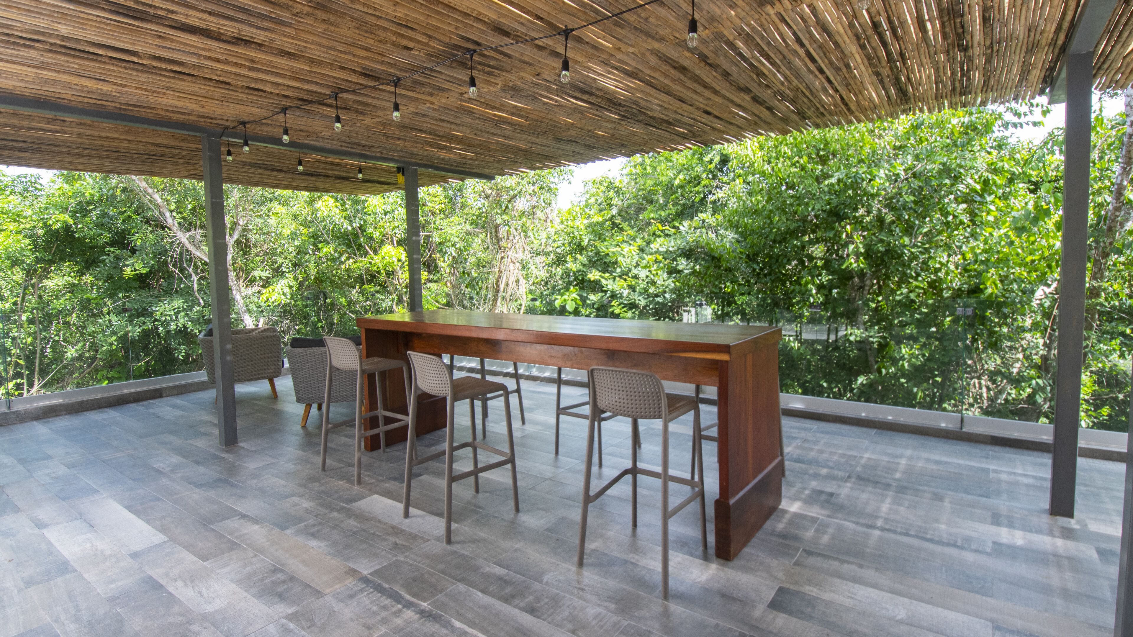 Une terrasse extérieure dotée d’un bar en bois et d’un espace salon, le tout entouré d’une végétation luxuriante.