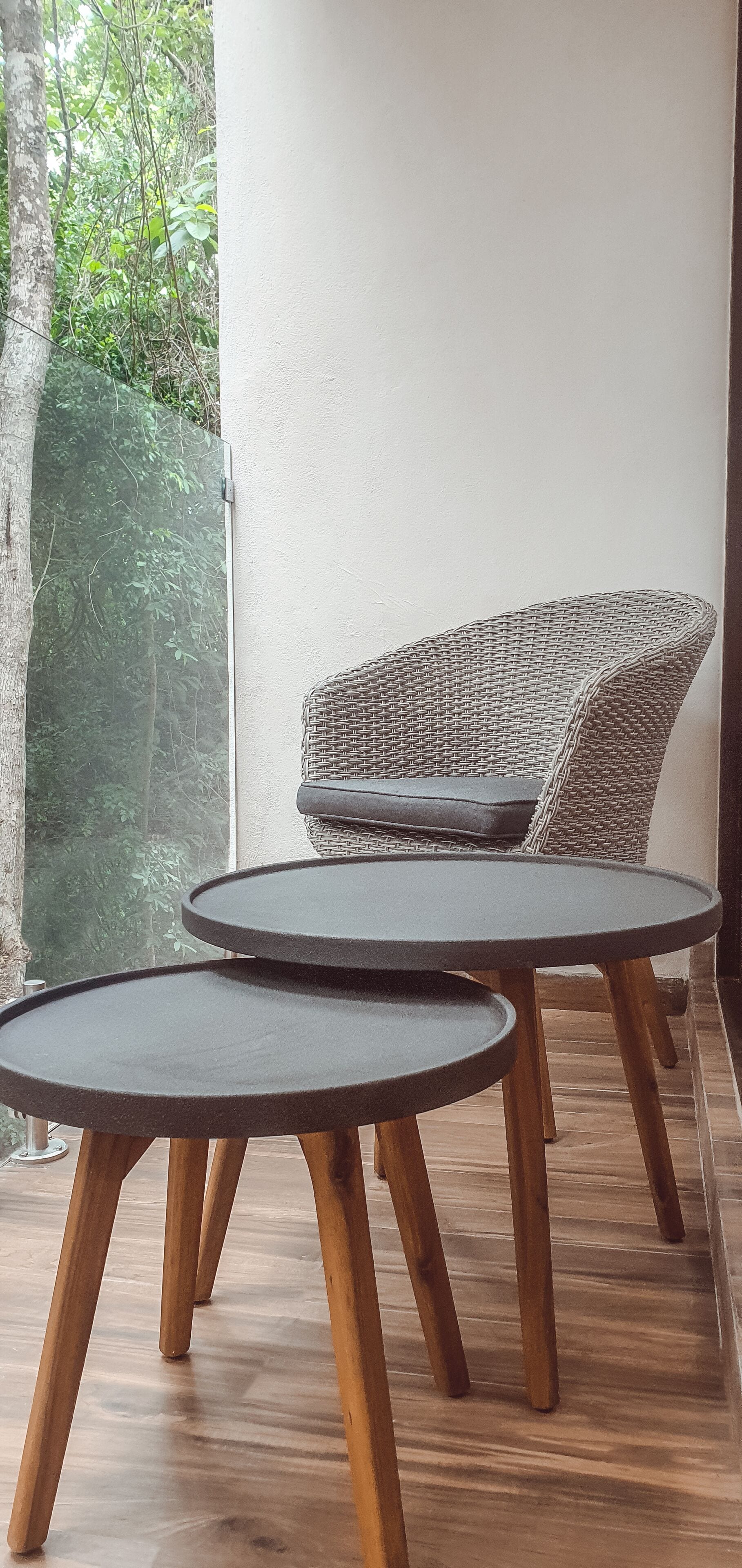 A wicker chair with a cushion and two round tables with wooden legs.