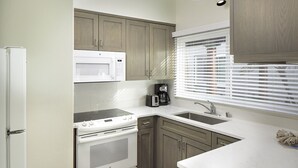 A compact kitchen with a built-in microwave, stove, and sink, wooden cabinets, and a window with blinds. - WCH at Wave Crest Resort (Del Mar)