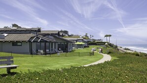 A coastal property with a paved walkway, a grassy lawn, and a view of the ocean. - WCH at Wave Crest Resort (Del Mar)
