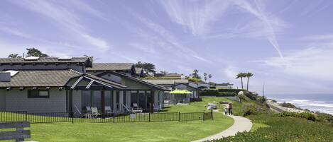 A coastal property with a paved walkway, a grassy lawn, and a view of the ocean.