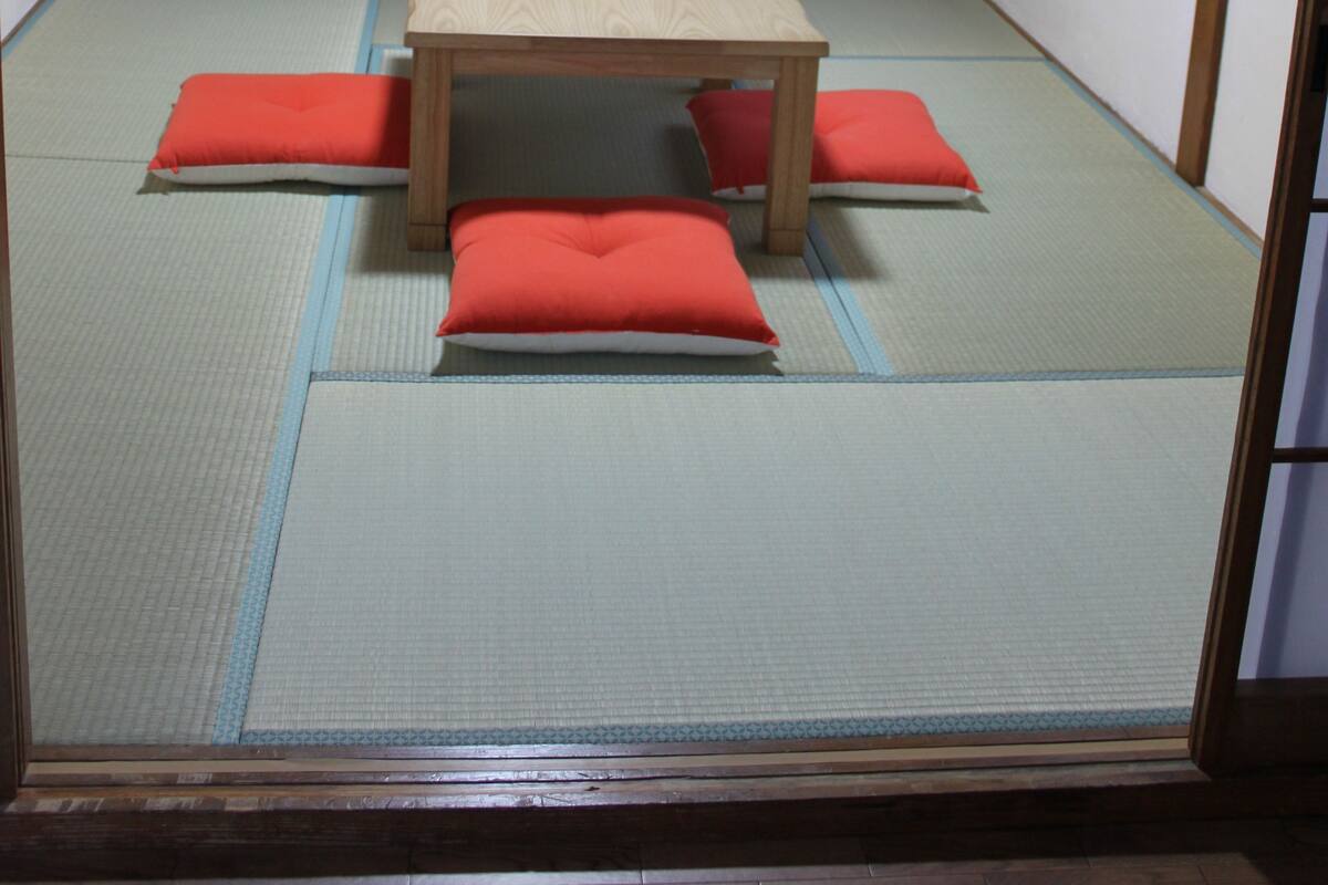 A traditional Japanese room with tatami flooring, a low wooden table, and red cushions.