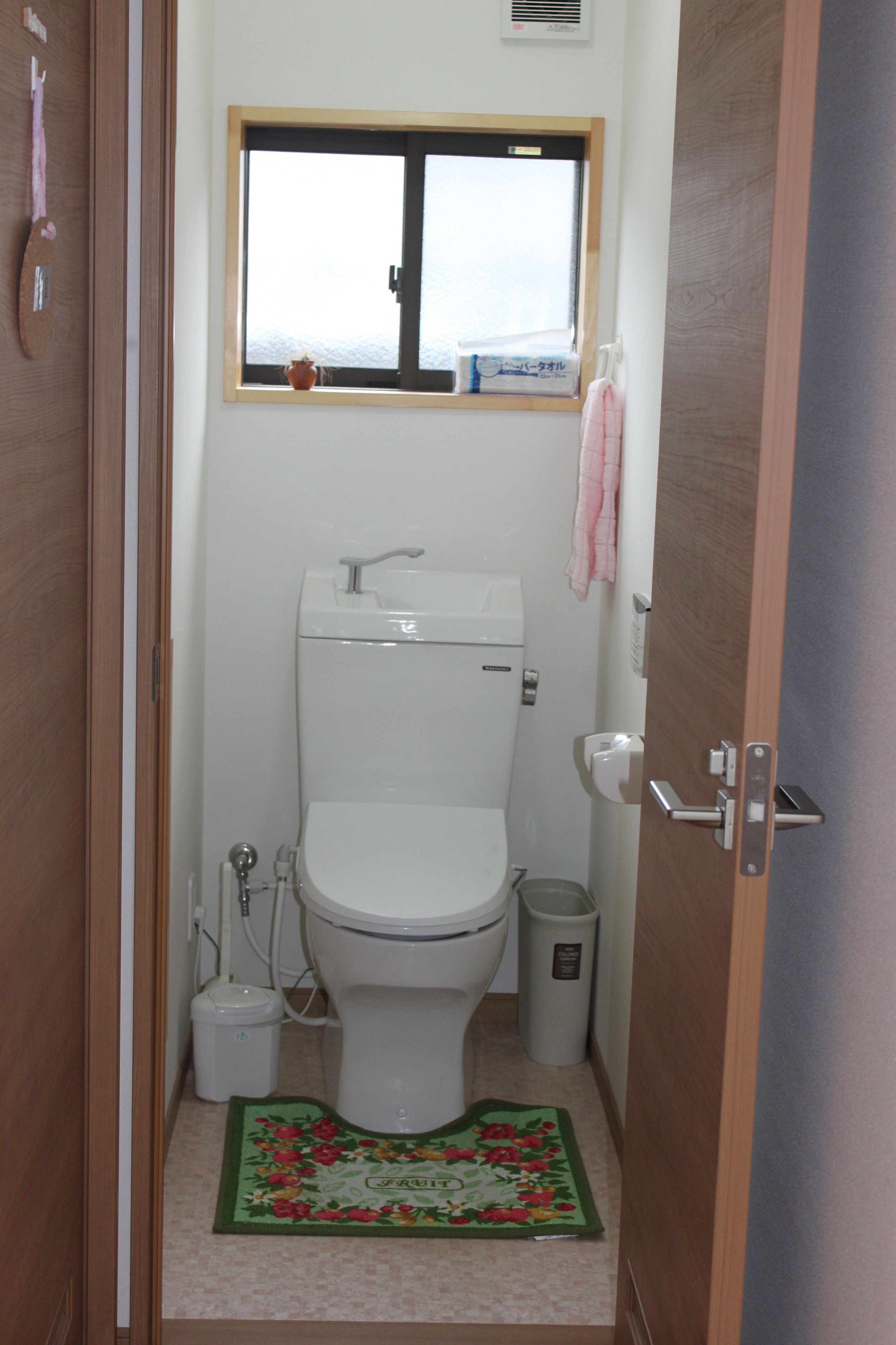 A small, clean bathroom with a toilet, a window, a sink, and a trash bin.