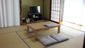 A traditional Japanese room with tatami flooring, a low wooden table, cushions, a television on a stand, and sliding doors. - ROSENCAT (Sado)