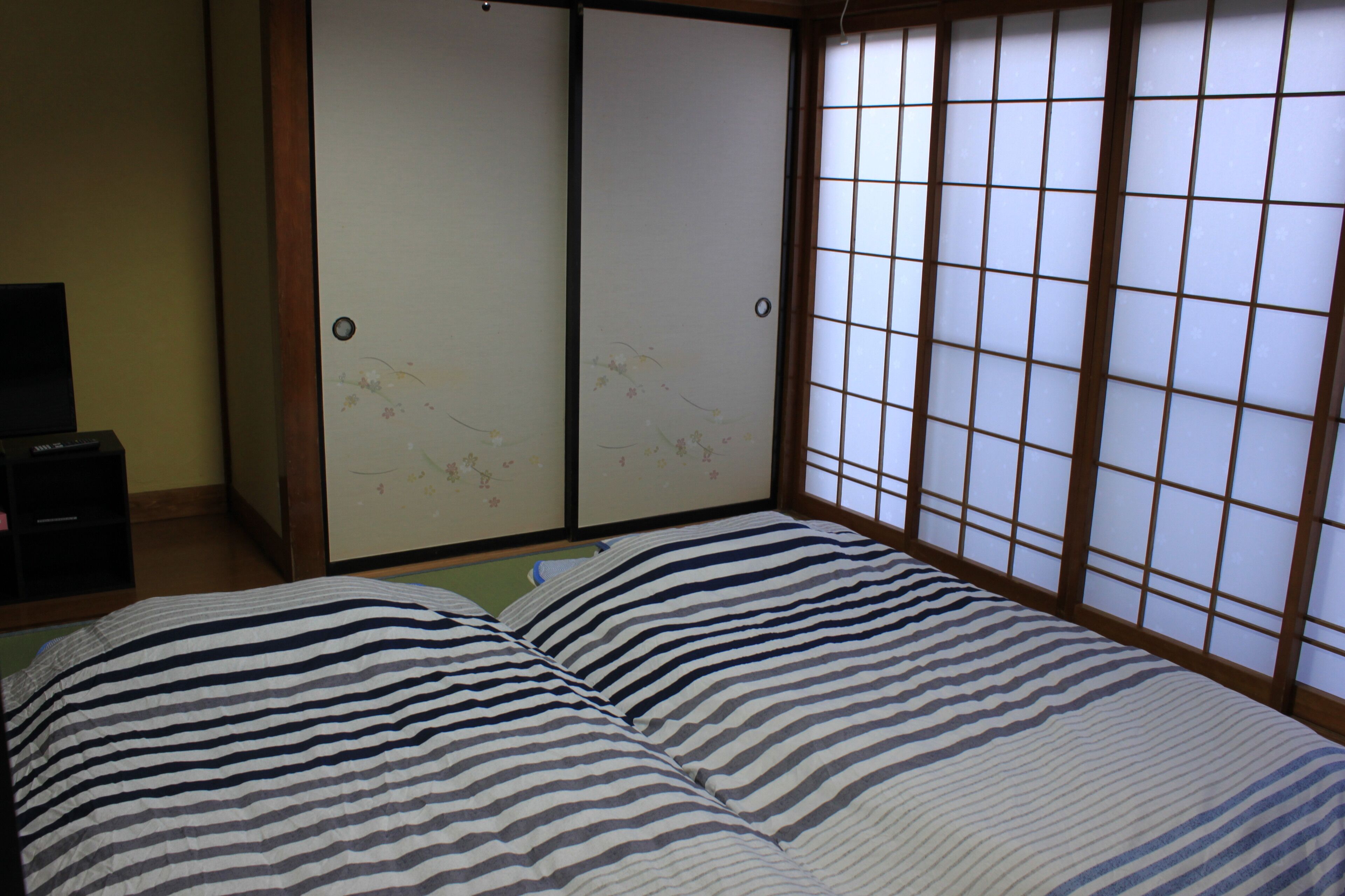 A room with a bed featuring striped bedding, a sliding shoji screen door, and a small black cabinet.