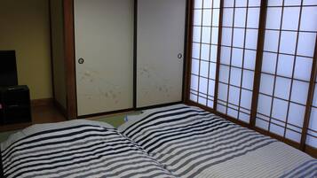 A room with a bed featuring striped bedding, a sliding shoji screen door, and a small black cabinet.