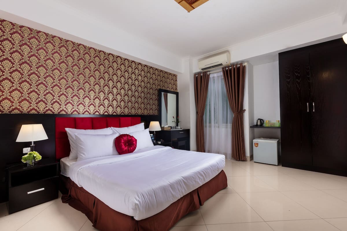 Une chambre d’hôtel avec un grand lit, une table de chevet avec une lampe, une commode, une armoire et une petite kitchenette.