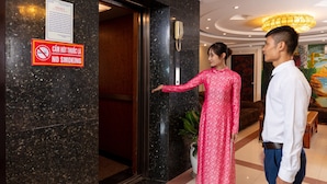 Een hotellobby met een marmeren receptiebalie, een bordje ‘niet roken’ en een vrouw in een roze jurk die bij de ingang staat.