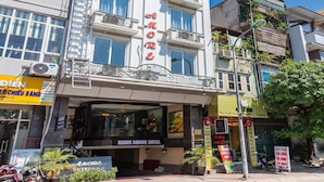 Een hotel met meerdere verdiepingen, balkons, een zichtbare ingang en borden met de naam Hanoi Amore Hotel.