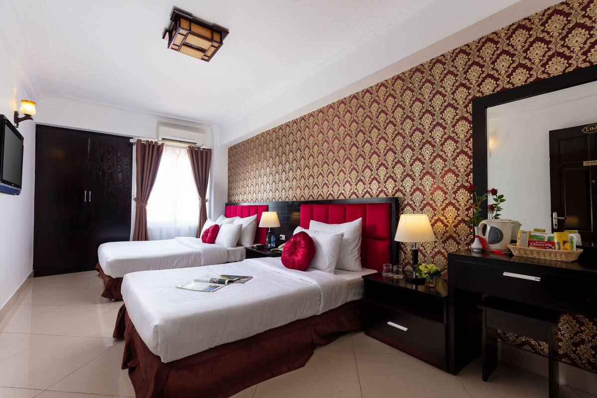 Une chambre d’hôtel avec deux lits, un grand miroir, une commode et un téléviseur.