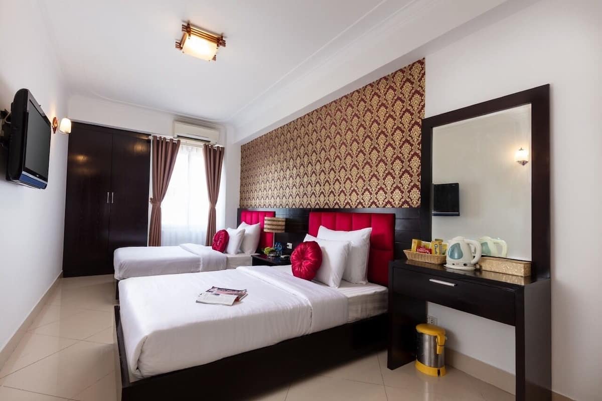 Une chambre d’hôtel avec deux lits, un grand miroir, une télévision et un bureau équipé d’une bouilloire et d’un service à thé.