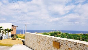 A coastal property with a stone wall, a wooden building, and a view of the sea. - isola villa kouri (Nakijin)