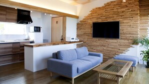 A modern living space with a kitchen, a sofa, a coffee table, and a TV mounted on a wooden wall. - isola villa kouri (Nakijin)