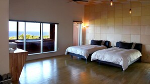 A spacious bedroom with two beds, a large window with a view of the ocean, a ceiling fan, and a floor lamp. - isola villa kouri (Nakijin)