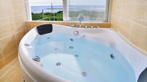 A large, freestanding bathtub with a view of the sea through a window. - isola villa kouri (Nakijin)