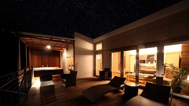 A spacious outdoor area with a wooden deck, a seating area with wicker furniture, and a view of the night sky. - isola villa kouri (Nakijin)