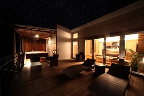 A spacious outdoor area with a wooden deck, a seating area with wicker furniture, and a view of the night sky. - isola villa kouri (Nakijin)