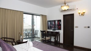 A hotel room with a bed, a desk, a chair, a TV, and a balcony with curtains.