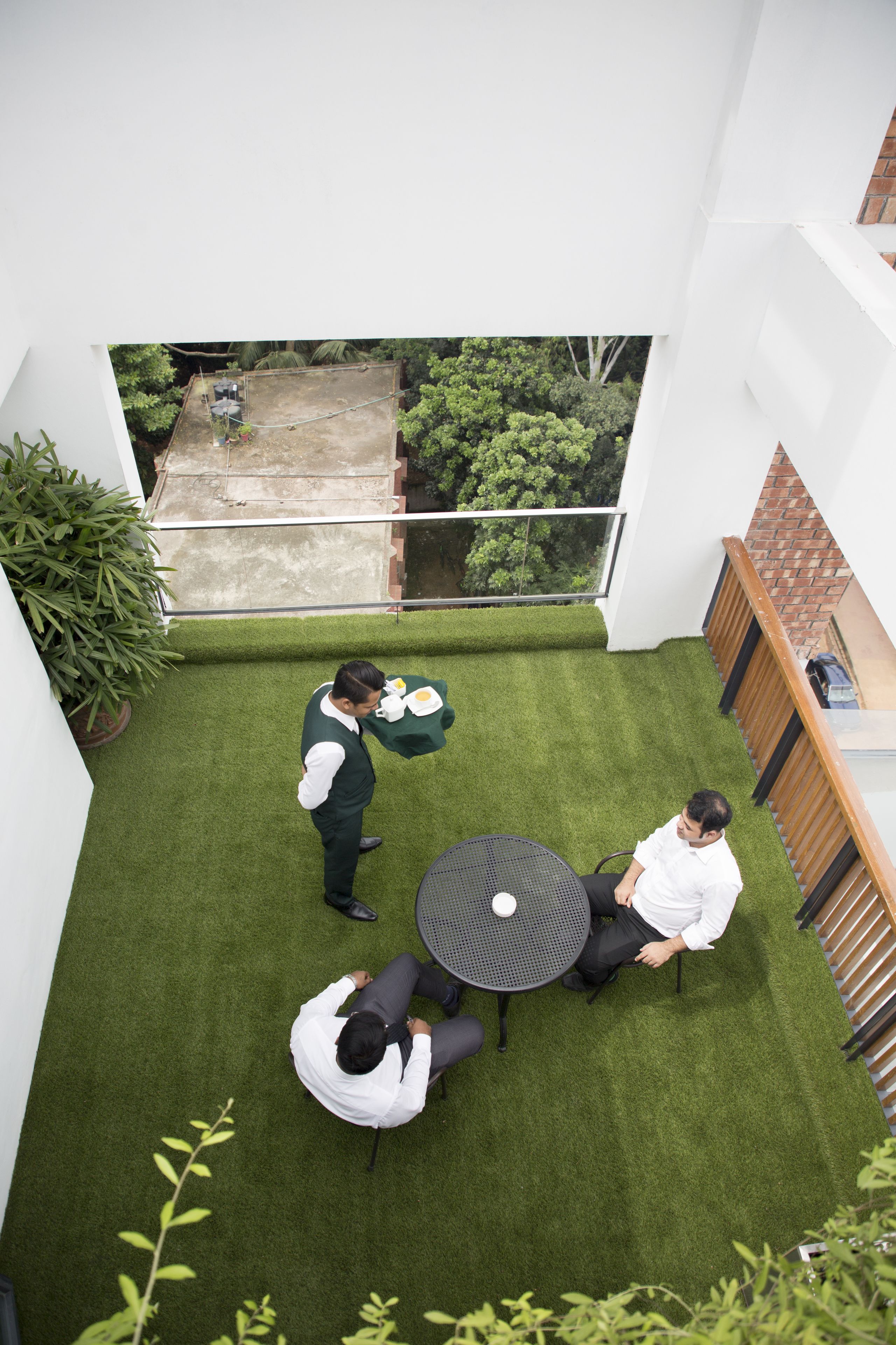 A rooftop terrace with a small table and chairs, surrounded by greenery and a view of the city.