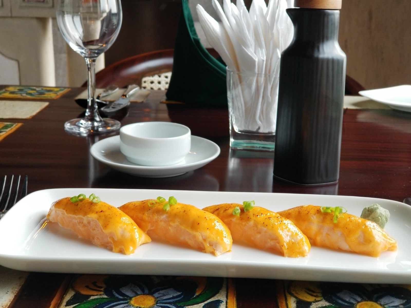 A dining table with a white plate of sushi, a glass of water, a white bowl, and a black vase.