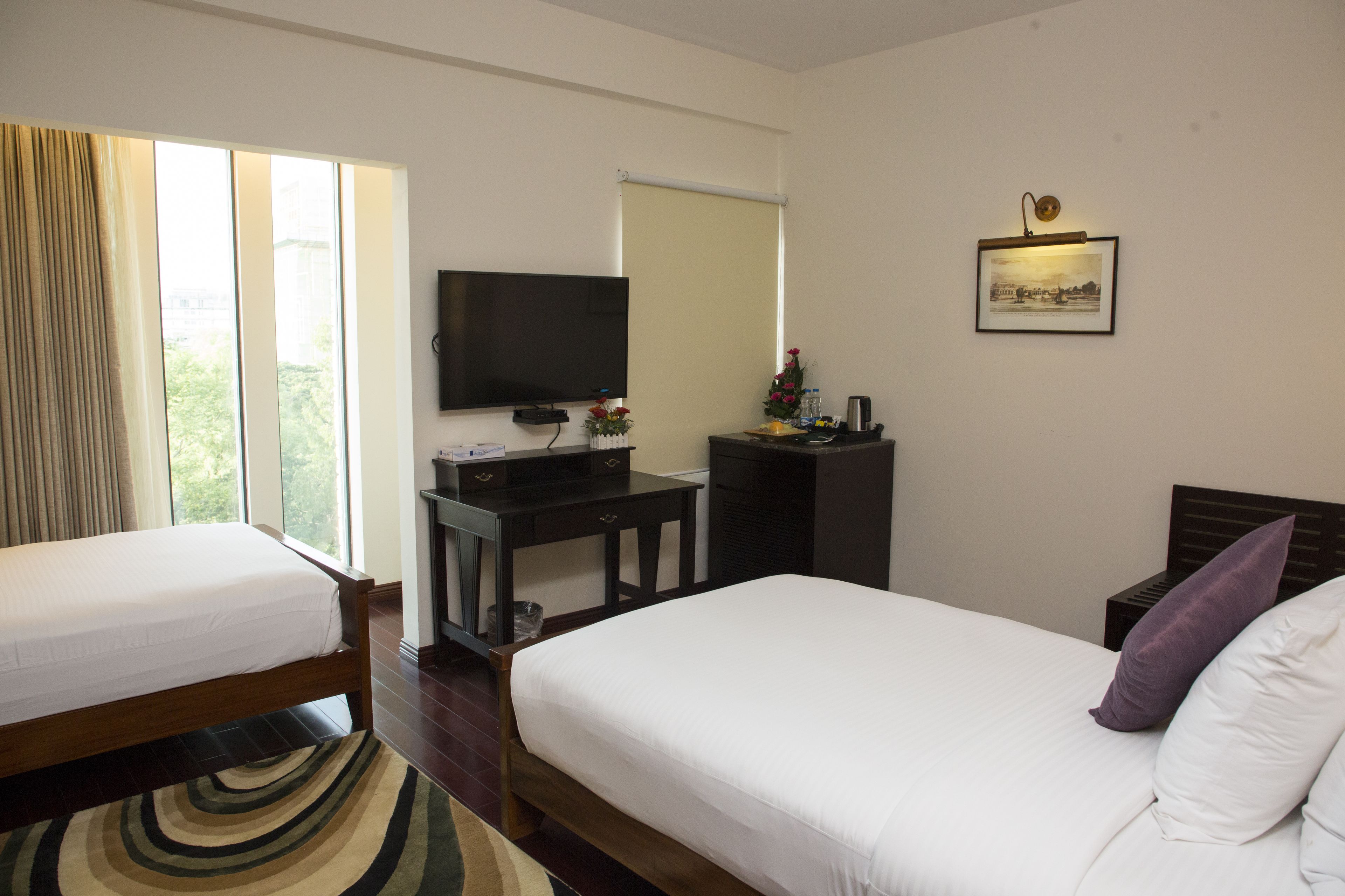 A hotel room with two beds, a flat-screen TV, a desk, and a large window with curtains.