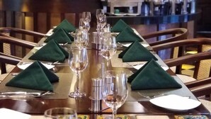 A restaurant setting with a long table set for a meal, featuring green napkins and multiple wine glasses.