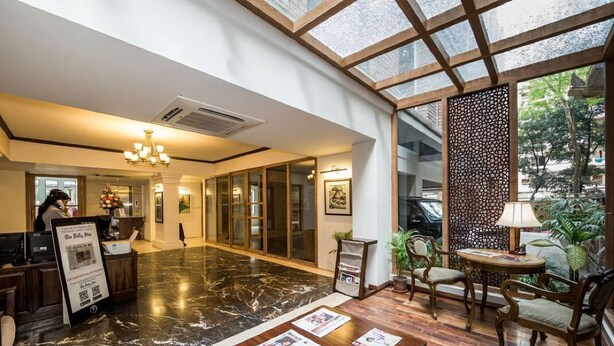 A hotel lobby with a marble floor, wooden furniture, a reception desk, and a large window with a view of greenery.
