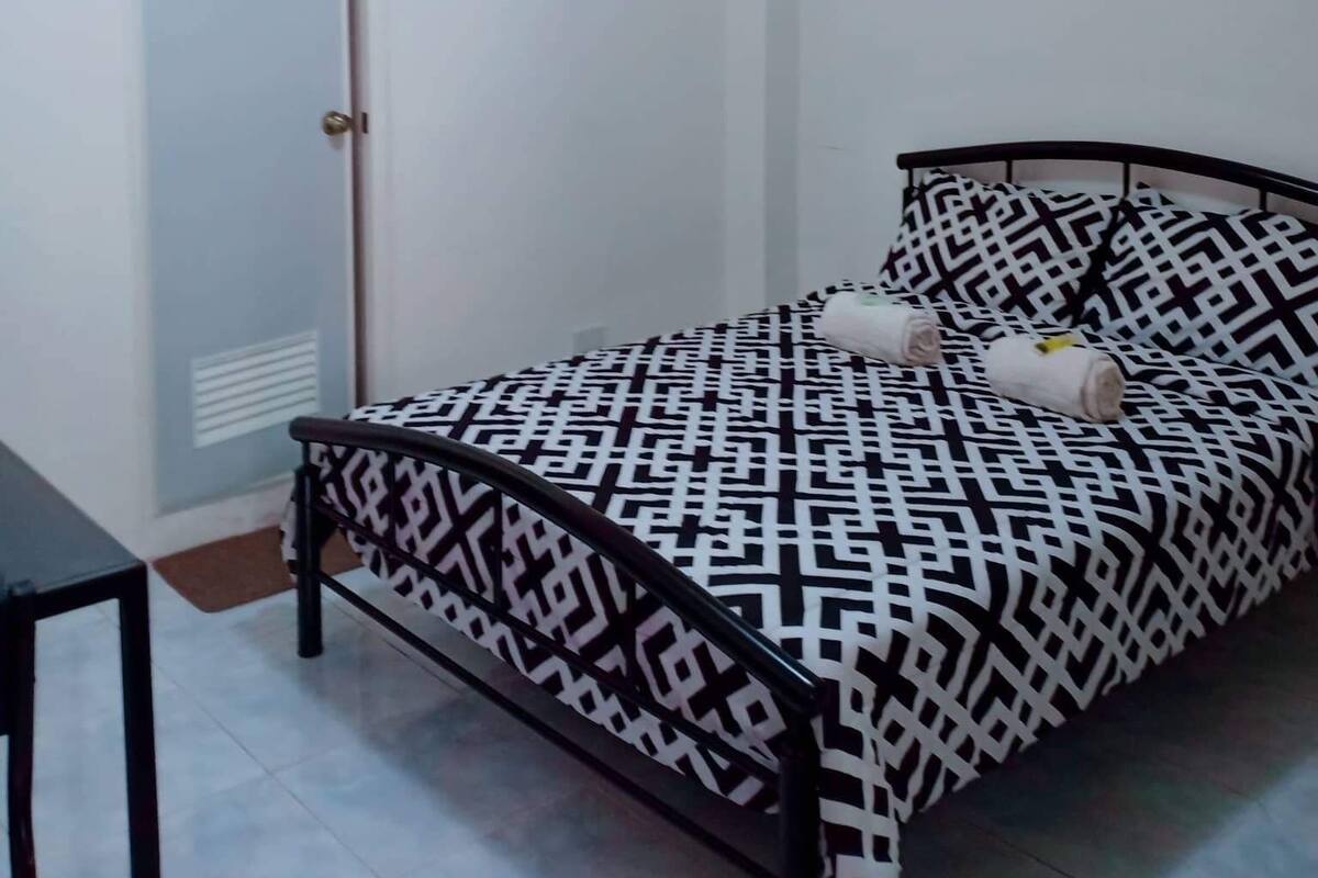 A bedroom with a bed, a door, a small table, and a framed picture on the wall.