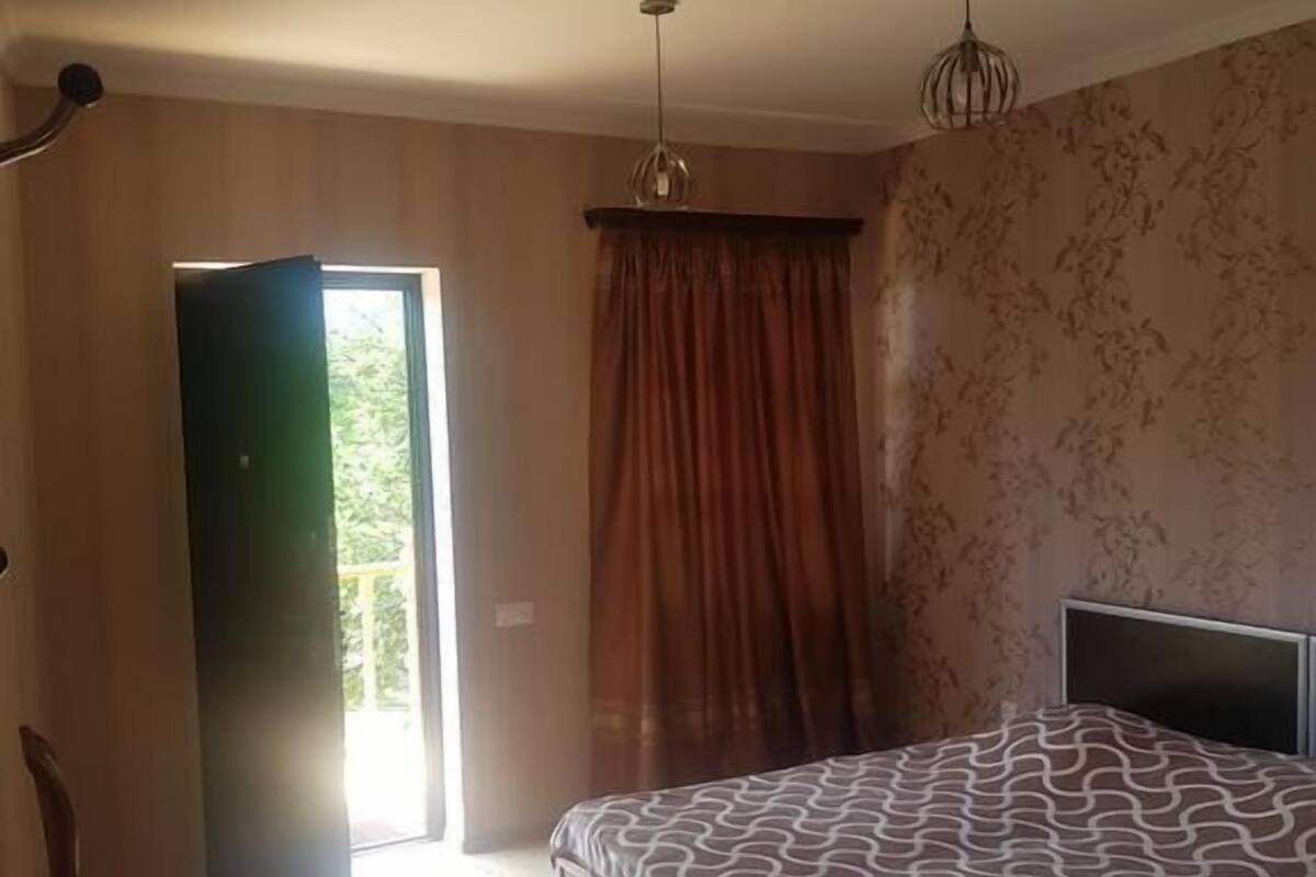 A bedroom with a bed, a chair, a window with curtains, and a door.