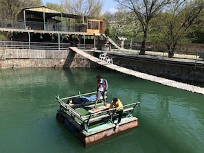 A small boat with two people on it, docked near a building with a balcony. - Amiran`s Lake (Tbilisi)