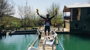 A wooden dock extending over a pool with a person standing on it, holding yellow objects. - Amiran`s Lake (Tbilisi)