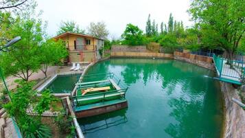 A swimming pool with a wooden boat docked, surrounded by a stone wall and greenery.