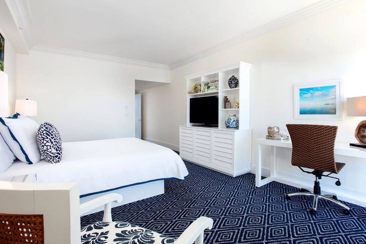 Habitación de hotel con cama, escritorio, silla, televisión y un cuadro en la pared.
