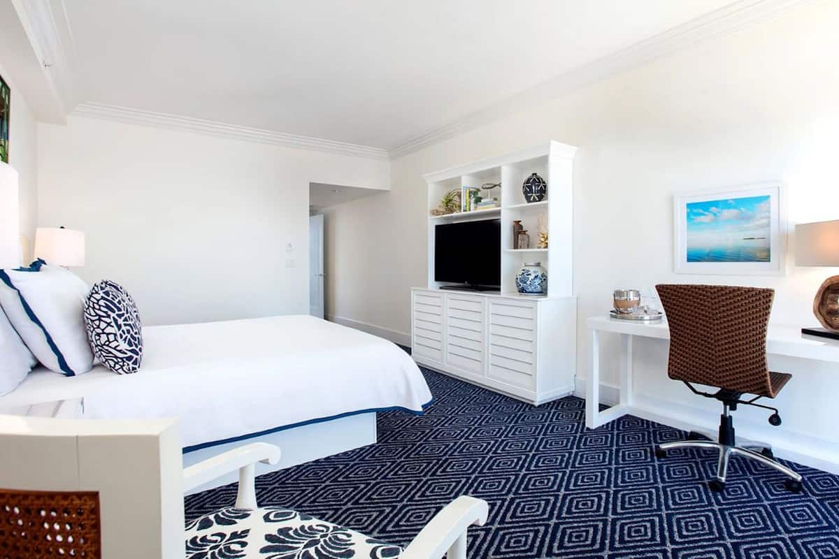 Habitación de hotel con cama, escritorio, silla, televisión y un cuadro en la pared.