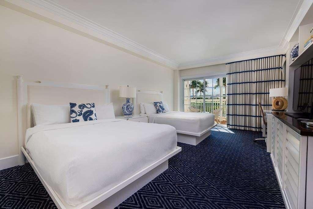 A hotel room with two beds, a large window, a balcony, and a minibar.