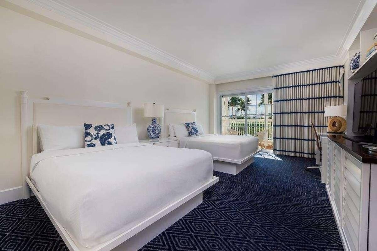 Habitación de hotel con dos camas, un ventanal grande, balcón y minibar.