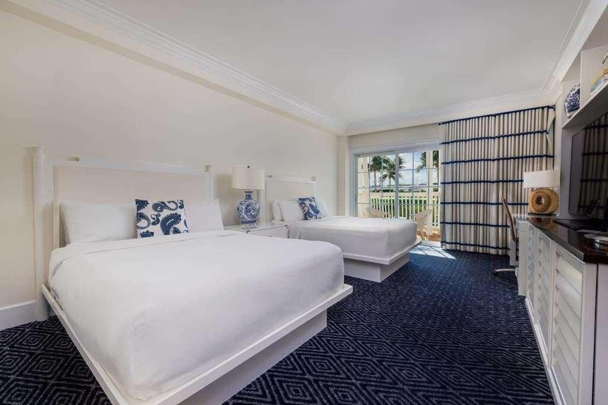 Habitación de hotel con dos camas, un ventanal grande, balcón y minibar.