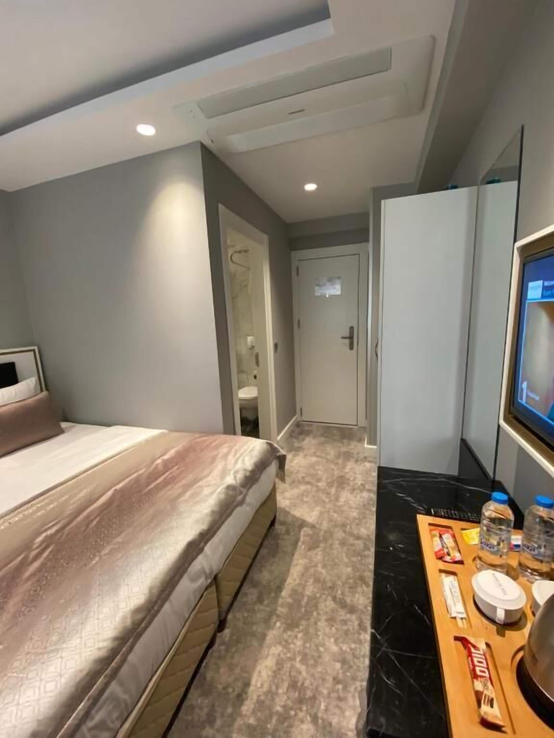 A hotel room with a bed, a TV, a minibar, and a bathroom visible through an open door.