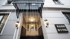 Entrada de hotel con un cartel que dice "KARE HOTEL", un juego de escalones y luces decorativas.