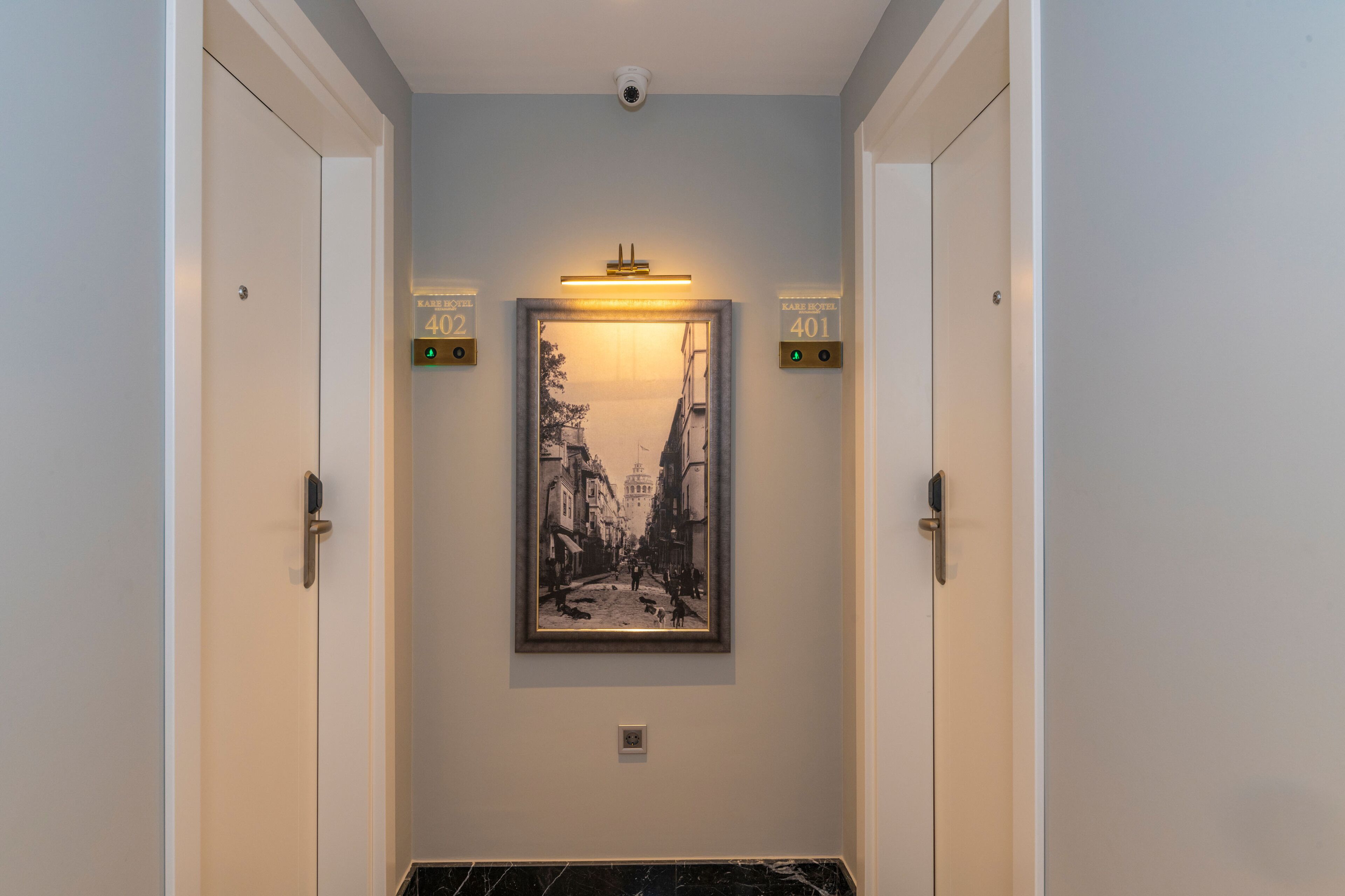 A hallway with a framed black and white photograph of a street scene, two doors labeled 402 and 401, and a security camera above.