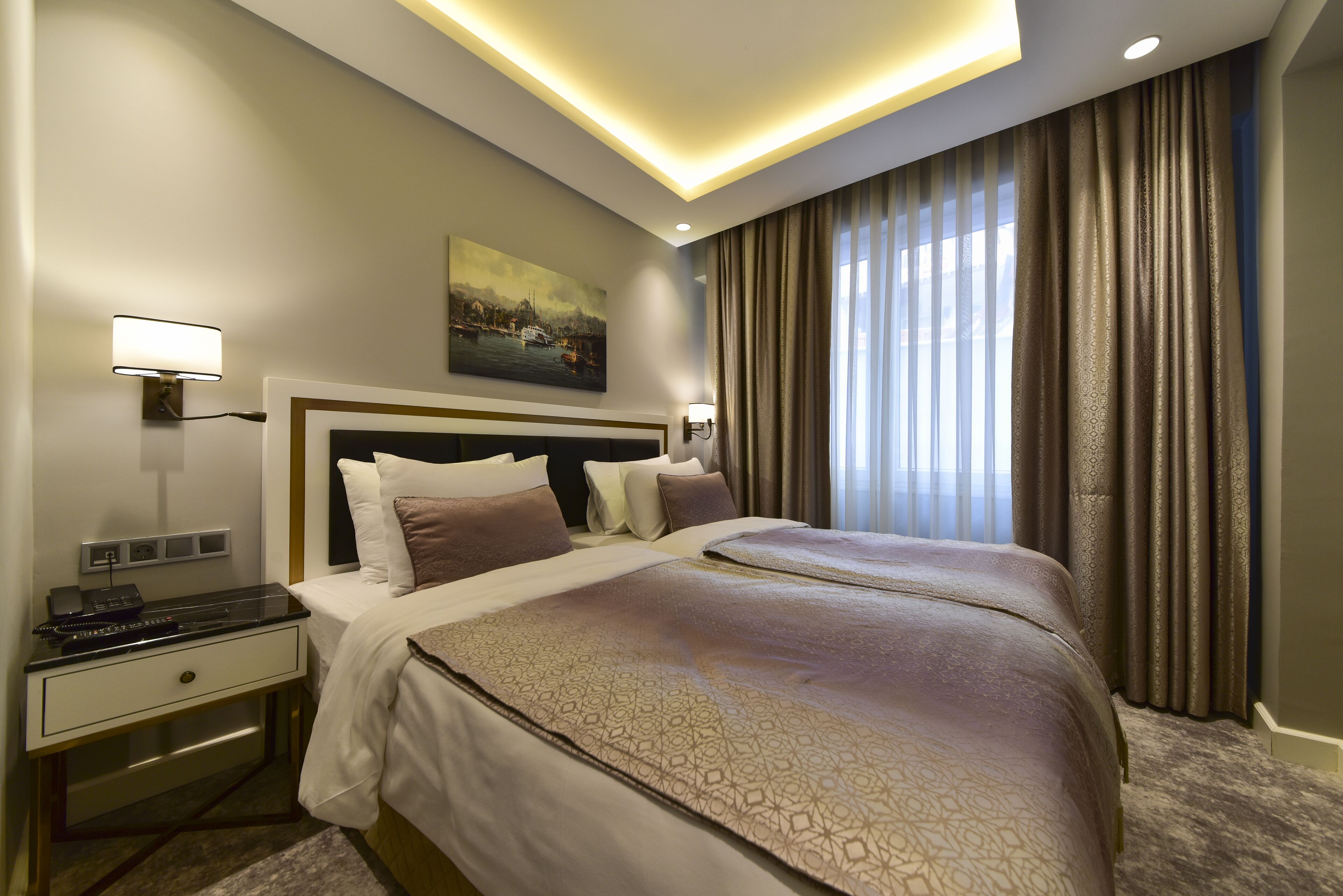 A hotel room with a large bed, two bedside tables, a desk with a lamp, and a painting on the wall.