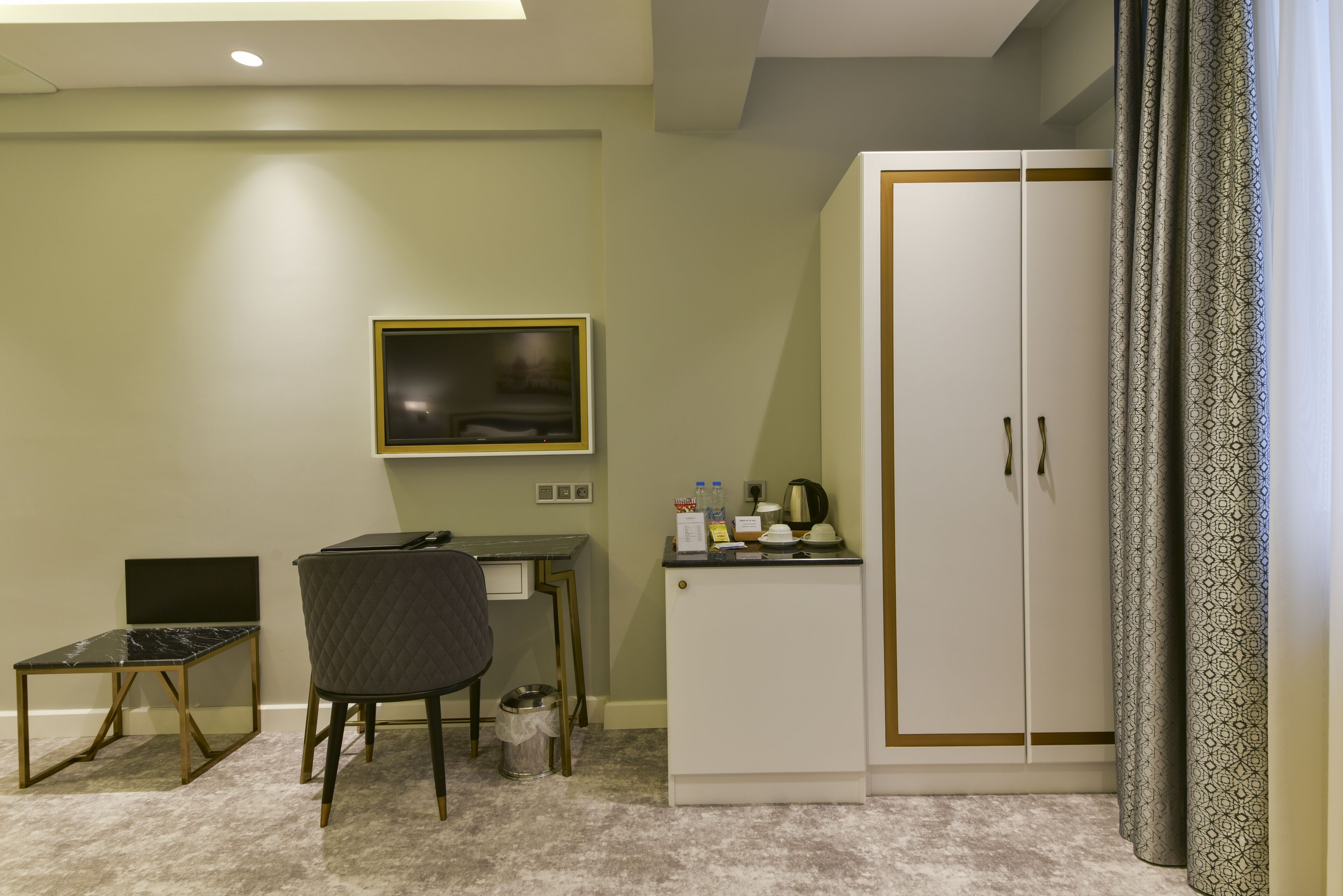 A hotel room with a bed, a desk with a chair, a wardrobe, a television, and a small cabinet with toiletries.